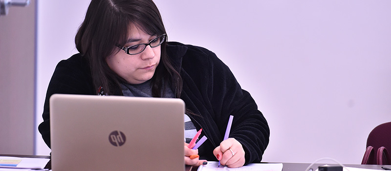 Female student writing on paper next to laptop
